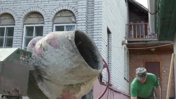 콘크리트는 집에서 일합니다 남자가 버킷에서 시멘트를 회전하는 콘크리트 믹서에 붓는다 — 비디오