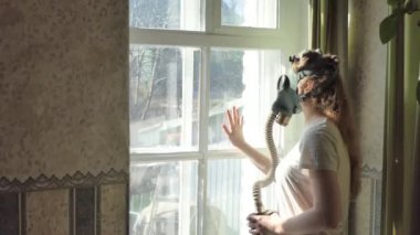 Enfeksiyon, kıyamet günü. Gaz maskeli genç bir kadın elini yavaşça pencerenin camına vuruyor..