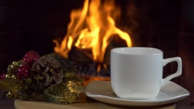 Noel, yeni yıl, şömine. Alevler ve Noel süslemeleriyle dolu küçük bir masanın üzerinde boş bir çay fincanı. Kapat..