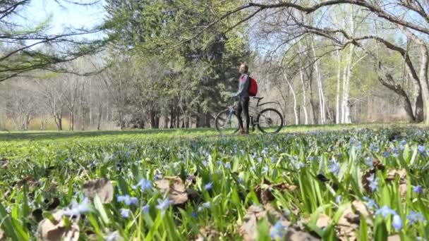 自我隔离 一个戴着医疗面具的自我隔离的女人带着她的自行车步行在花木之间的公园里 — 图库视频影像
