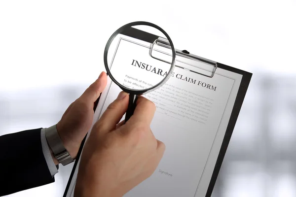 man looking through a  magnifying glass  to the Blank insurance claim form