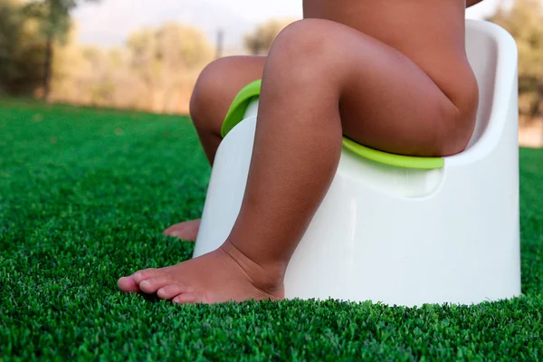 Children's legs hanging down from a chamber-pot on a green background — Stock Photo, Image