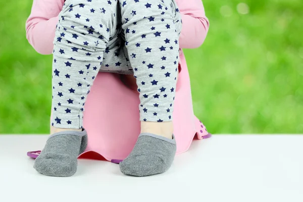 Dětské nohy visí dolů ze nočník na zeleném pozadí — Stock fotografie