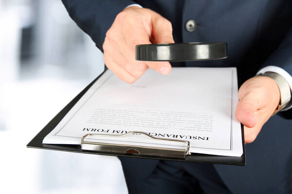 человек смотрит через увеличительное стекло на бланк заявления о страховом возмещении
 