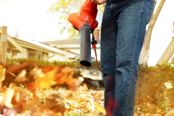 Man working with  leaf blower: the leaves are being swirled up and down on a sunny day — Stock Photo, Image