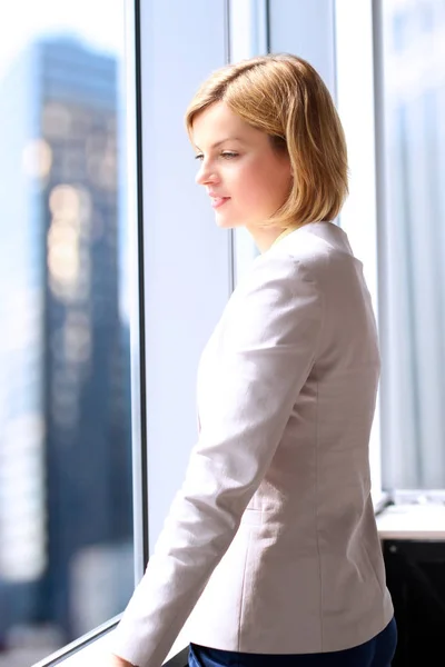 Successful businesswoman standing near a window. Downtown background behind — Stock Photo, Image