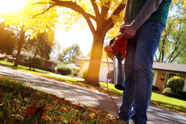 Man working with  leaf blower: the leaves are being swirled up and down on a sunny day — Stock Photo, Image