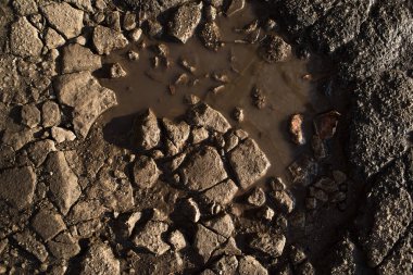 Yol yüzeyinde taşlar olan küçük kirli bir su birikintisi. Yağmurdan sonra antenatal kapak kırıldı