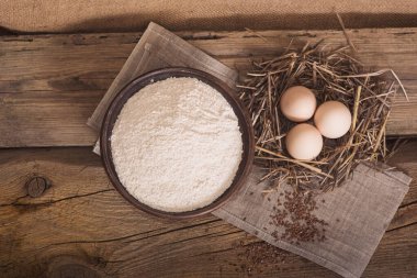 Çavdar unuyla ahşap bir masaya samanla sarılmış tavuk yumurtaları. Pişirme ve pişirme malzemeleri.