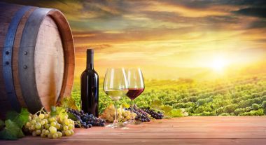 Wine Glasses And Bottle With Barrel In Vineyard At Sunset