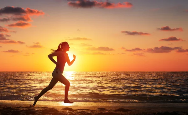 Жінка біжить на пляжі під час заходу сонця — стокове фото