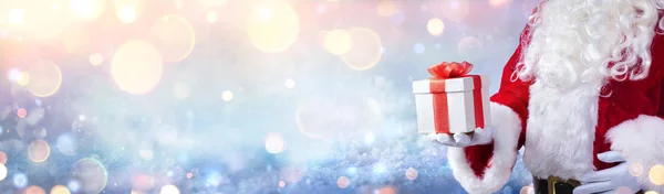 Jultomten Håller Julklapp Med Snöig Bakgrund Och Gyllene Ljus — Stockfoto