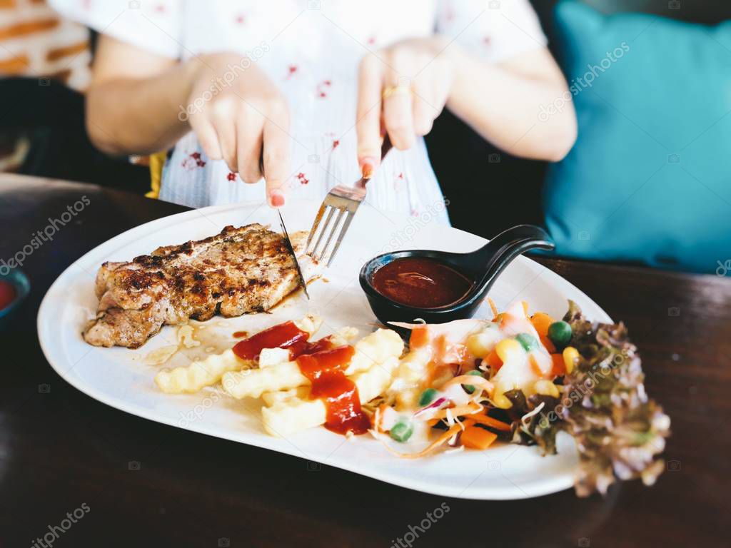 lady eating delicious steak in restaurant. Only hands, woman holding fork and knife and tasting meat with grill vegetables.