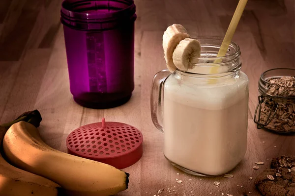 protein shake in a drinking glass with bananas, oatmeal and oatmeal cookies