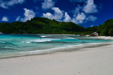 Turistler güzel kumsalda vakit geçiriyorlar - Baie Lazare plajı, Mahe Adası, Seyşeller. Palmiye ağaçları kumları dalgaları çarpıyor. Güzel kıyı mavi gökyüzü ve turkuaz su..