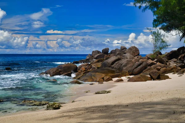 Ocean waves and granite rocks - Takamaka beach, Mahe Island, Seychelles.Palmtrees, sand, crashing waves, beautiful shore, blue sky and turquoise water.