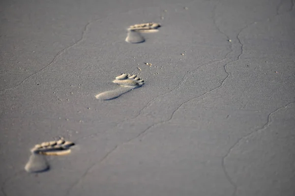 3 footprints on the grey sand, wide shot. Text space on right.