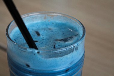 Bir bardak buzlu bezelye latte mavi çay kokteyli. Tahta masa üzerinde siyah saman ve buzlu süt.