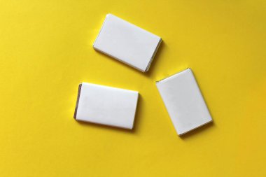 Gümüş folyoya sarılı çikolatalar ve sarı yüzeyde izole edilmiş beyaz boş kağıtlar.