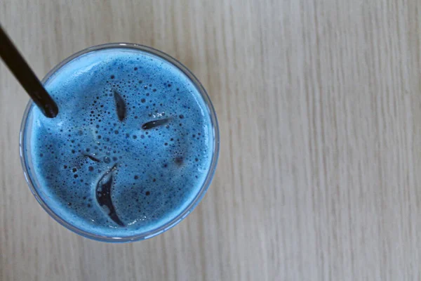 Ποτήρι παγωμένου καφέ latte blue tea cocktail με γάλα σε ξύλινο τραπέζι με μαύρο καλαμάκι και πάγο — Φωτογραφία Αρχείου