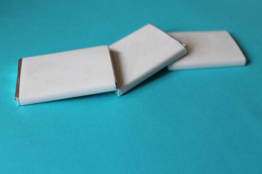 Gümüş folyoya sarılı çikolatalar ve mavi yüzeyde izole edilmiş beyaz kağıtlar.