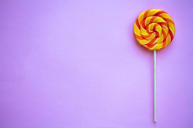 Mor zemin üzerinde parlak girdaplı lolipop ve fotokopi alanı. Renkli bükülmüş şekerlerle şenlikli bir arka plan. Gök kuşağı tatlı çubukta