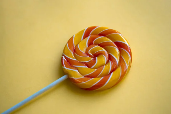 Sarı arka planda parlak kıvrımlı lolipop. Renkli bükülmüş şekerlerle şenlikli bir arka plan. Yaklaş gökkuşağının etrafındaki tatlı çubuğa.