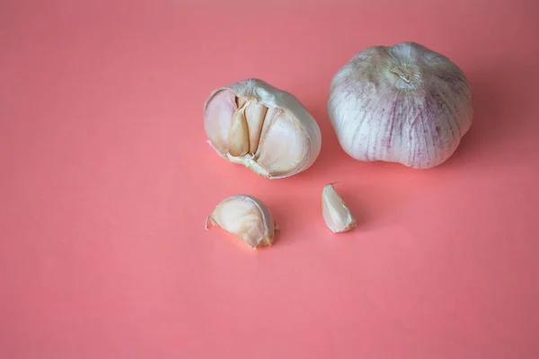 Yumuşak pembe arka planda iki sarımsak soğanı ve karanfil. Mevsimlik sebzeleri kapatın. Taze organik sağlıklı yiyecekler. Baharatlı mutfak malzemesi. Kopya boşluğu ile arkaplan hasat ediliyor