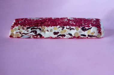 Torrone ya da fındıklı ve kırmızı kuru meyveli nougat bar. Geleneksel İtalyan tatlıları pembe arka planda kapanıyor. Tatlı ve sağlıklı yiyecekler.