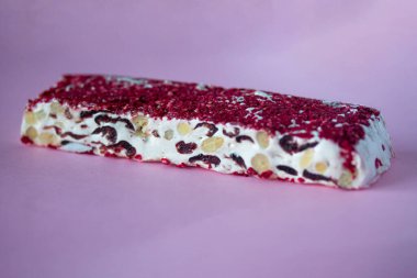 Torrone ya da fındıklı ve kırmızı kuru meyveli nougat bar. Geleneksel İtalyan tatlıları pembe arka planda kapanıyor. Tatlı ve sağlıklı yiyecekler.