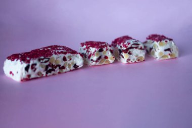 Torrone ya da fındıklı ve kırmızı kuru meyveli nougat bar. Geleneksel İtalyan tatlıları pembe arka planda kapanıyor. Tatlı ve sağlıklı yiyecekler.