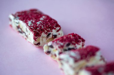 Torrone ya da fındıklı ve kırmızı kuru meyveli nougat bar. Geleneksel İtalyan tatlıları pembe arka planda kapanıyor. Tatlı ve sağlıklı yiyecekler.