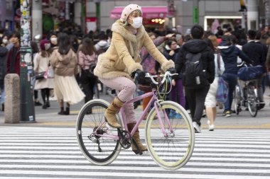 Tokyo, Japonya, 22 Şubat 2020 - Bulaşıcı hastalıkları önlemek için cerrahi maske takan bir kadın Shibuya 'nın ünlü geçidinde bisiklet sürüyor. Japonya, ülkede koronavirüs enfeksiyonu vakalarını doğruladı.