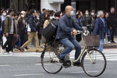 Tokyo, Japonya, 22 Şubat 2020 - Bulaşıcı hastalıkları önlemek için cerrahi maske takan bir adam Shibuya 'nın ünlü geçidinde bisiklet sürüyor. Japonya, ülkede koronavirüs enfeksiyonu vakalarını doğruladı.