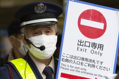 Tokyo, Japonya, 22 Şubat 2020 - Bulaşıcı hastalıkları önlemek için cerrahi maske takan Shibuya İstasyonu personeli istasyonun çıkışında bir tabela tutuyor. Japonya, ülkede koronavirüs enfeksiyonu vakalarını doğruladı.