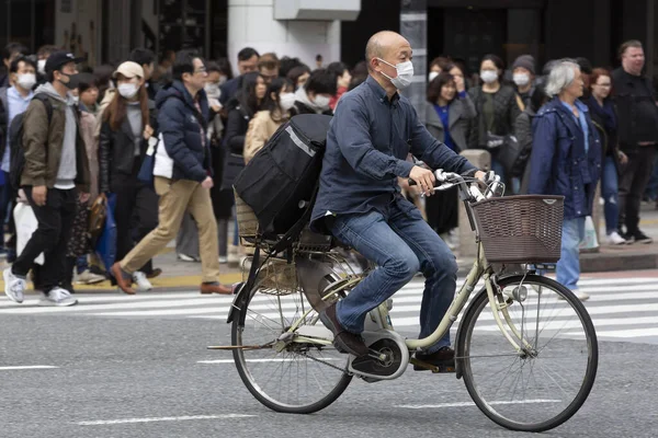 Tokyo, Japonya, 22 Şubat 2020 - Bulaşıcı hastalıkları önlemek için cerrahi maske takan bir adam Shibuya 'nın ünlü geçidinde bisiklet sürüyor. Japonya, ülkede koronavirüs enfeksiyonu vakalarını doğruladı.