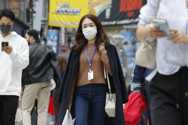 Tokyo, Japonya, 28 Mart 2020 - Bulaşıcı hastalıkları önlemek için cerrahi maske takan bir kadın Ginza alışveriş bölgesinde yürüyor.