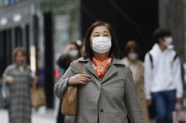 Tokyo, Japonya, 28 Mart 2020 - Bulaşıcı hastalıkları önlemek için cerrahi maske takan yaşlı bir kadın Ginza alışveriş bölgesinde yürüyor.