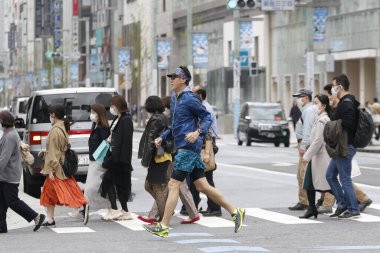 Tokyo, Japonya, 28 Mart 2020 Ginza alışveriş bölgesindeki bulaşıcı hastalıkları önlemek için cerrahi maske takan bir adam koşarak yayaların yanından geçiyor..