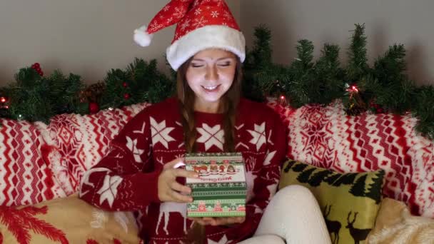 Menina feliz no chapéu de Papai Noel abre uma caixa de presente de Natal com luz mágica dentro — Vídeo de Stock