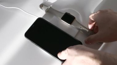 Erkek eli cep telefonunu ve kablosuz şarjdan akıllı saatleri çıkarır.
