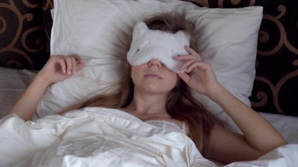 Lazy young woman with blindfold on eyes wakes up in her bed late in the morning — Stock Video