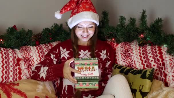 Menina feliz no chapéu de Papai Noel abre uma caixa de presente de Natal com luz mágica dentro — Vídeo de Stock