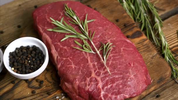 Rohe, frische Steaks mit Rosmarin und Kräutern auf rustikalem Holzbrett serviert — Stockvideo