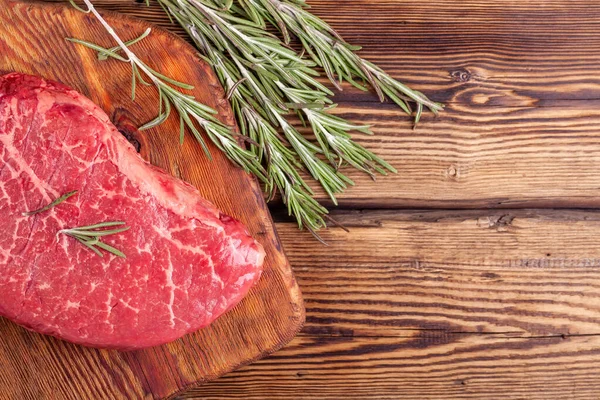 Raw Fresh Rib Eye Steak Served with Rosemary and Herbs on Rustic Wooden Board