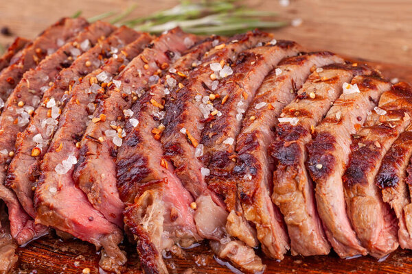 Close Up of Chopped Grilled Steak Rib Eye on Rustic Cutting Board on Wooden Background. Juicy Medium Ribeye Steak with Spices and Rosemary. Concept of Delicious Meat Food