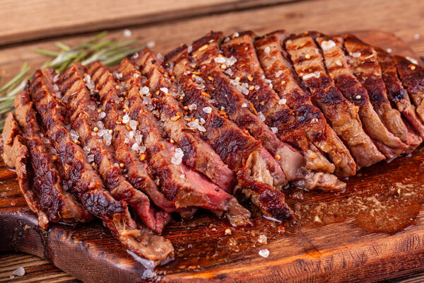 Close Up of Chopped Grilled Steak Rib Eye on Rustic Cutting Board on Wooden Background. Juicy Medium Ribeye Steak with Salt, Pepper and Rosemary. Concept of Delicious Meat Food