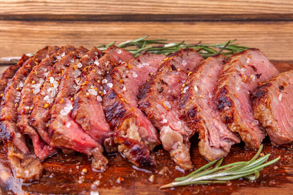 Chopped Grilled Steak Rib Eye on Rustic Cutting Board on Wooden Background. Juicy Medium Ribeye Steak with Spices and Rosemary. Concept of Delicious Meat Food