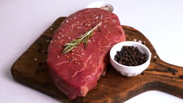 Steak de boeuf frais cru servi avec du romarin, du sel et du poivre sur du bois rustique — Video