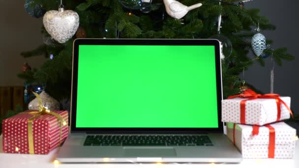 圣诞礼盒和圣诞树中的桌面上有绿色屏风的笔记本电脑 — 图库视频影像